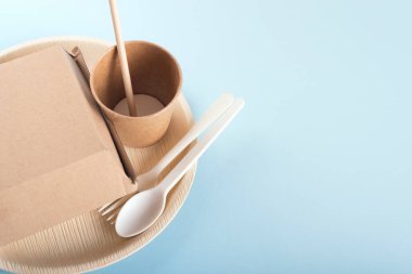 Açık mavi arka planda tek kullanımlık tabak, fincan, çatal, kaşık, saman ve burger kutusu.