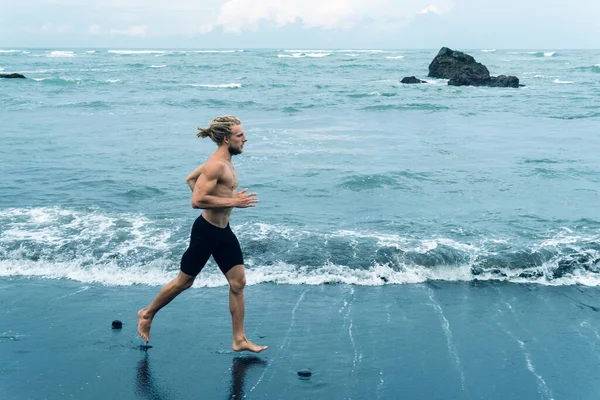 Atleet man joggen op een zwart zand strand — Stockfoto