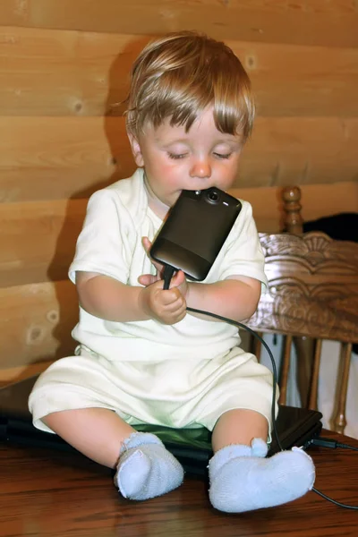 Bebê Menino Senta Uma Mesa Laptop Detém Telefone Celular Sua — Fotografia de Stock