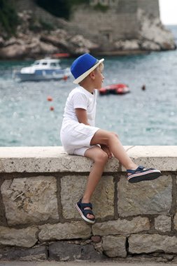 mavi şapkalı çocuk parapet ve lo katlanmış bacağı ile oturur