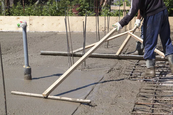 Рабочие выравнивают свежую бетонную плиту специальными деревянными рабочими — стоковое фото
