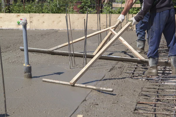 Рабочие выравнивают свежую бетонную плиту специальным рабочим инструментом — стоковое фото