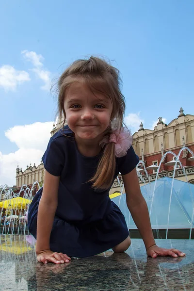 Sorridente ragazza seduta alla fontana nella piazza di Cracovia e — Foto Stock
