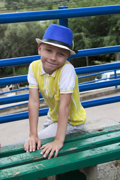 Lächelnder Junge mit Hut sitzt auf einer Bank — Stockfoto