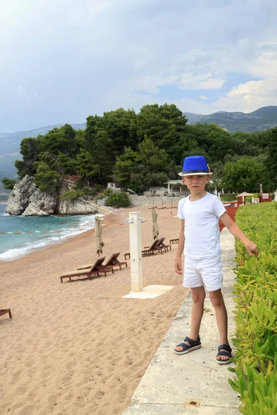 Menino de chapéu azul caminha na praia em Milocher Park perto de Budva , — Fotografia de Stock