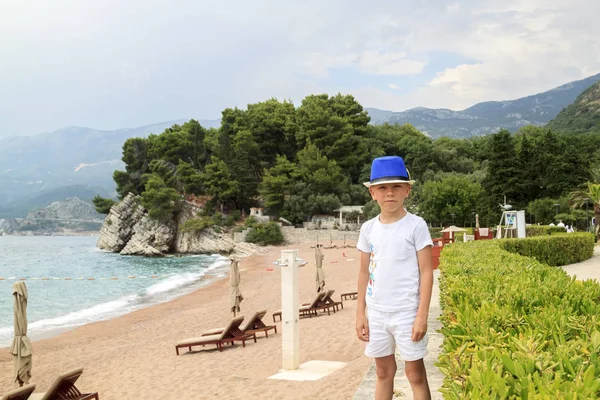 Menino de chapéu azul caminha na praia em Milocher Park perto de Budva , — Fotografia de Stock