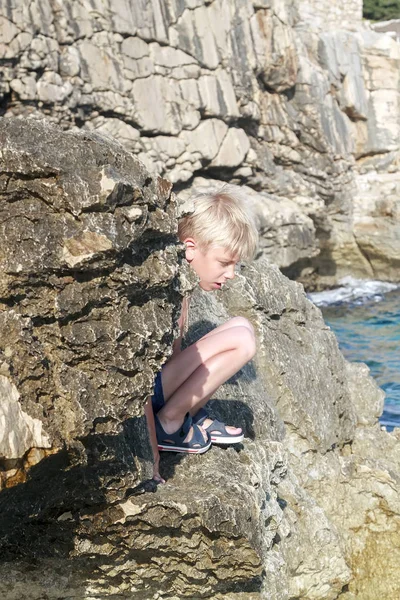 Niedlich gebräuntes und sonnengebranntes Haar Junge sitzt auf dem Rand eines Stee — Stockfoto