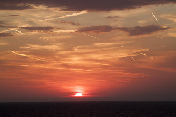 Beautiful view of the sun hiding behind the sea surface. the sunset sky is orange with clouds and condensation traces