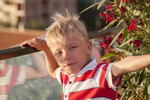 Blond boy looks at the camera and throws his hand up with a vict — Stock Photo, Image