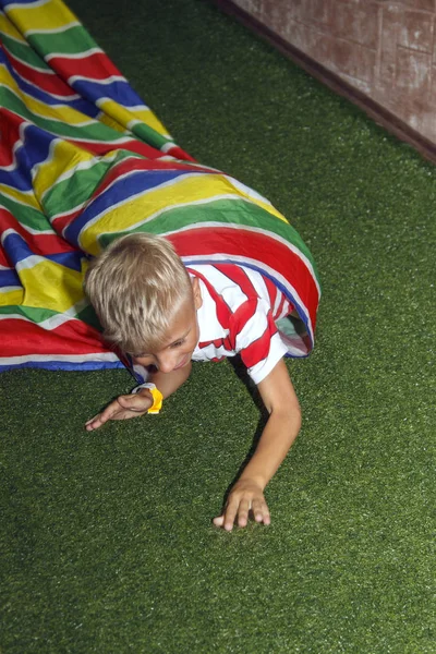 Blond boy play crawling through tube in kids zone in amusement p — Stock Photo, Image