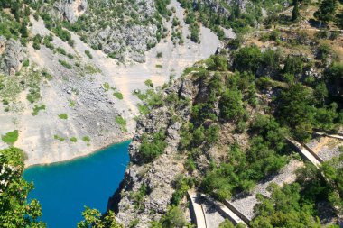 Imotski şeffaf derin mavi karst gölüne dağın dik yamacından aşağı dolambaçlı yol