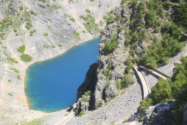 Imotski şeffaf derin mavi karst gölüne dağın dik yamacından aşağı dolambaçlı yol