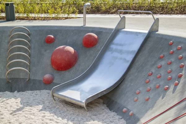 Moderner Spielplatz mit Metallrutsche in zeitgenössischem Landschaftsdesign, Treppe aus roten Halbkugeln am Hang eines Betonhügels — Stockfoto