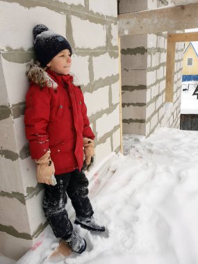 Kırmızı ceketli mutlu çocuk kışın inşaat halindeki binanın çatısında duruyor.