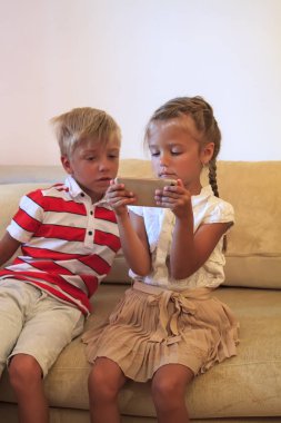 Çocuklar akıllı telefon ekranına bakın. Çocuk telefona bakar ve mutlu kız kardeşine bakar.