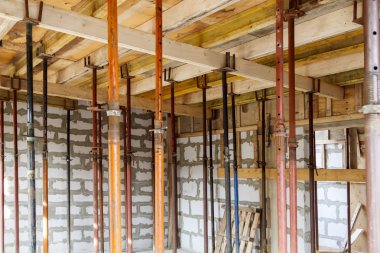 Metalik tutucularla ahşap biçimlendirme manzarası, köpük bloktan inşaat halindeki kır evindeki katlar arasında çakışacak.