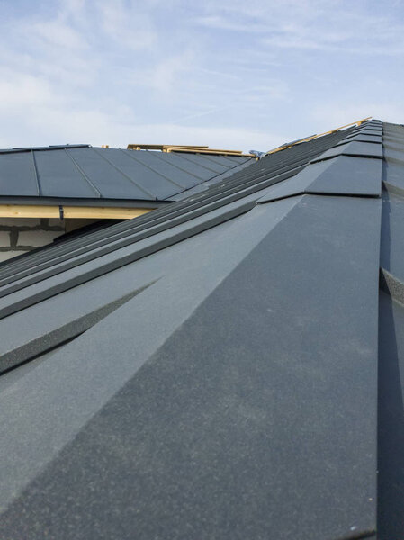 крупный план строительных лесов и строящегося дома с серой складной крышей на гидроизоляционном слое
