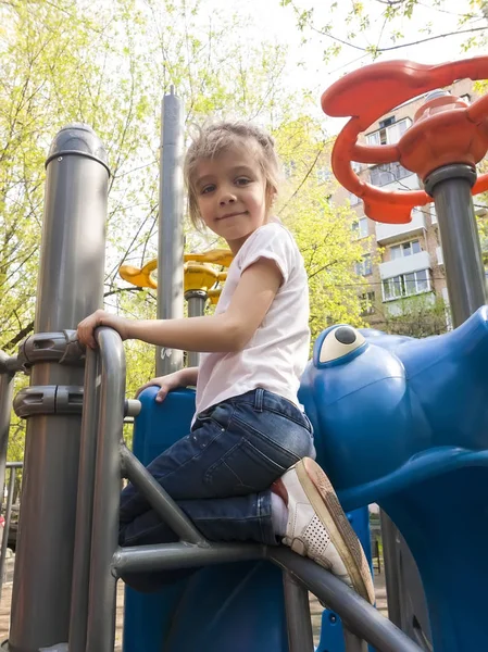 Menina feliz sentado no parque infantil na primavera e olha para — Fotografia de Stock