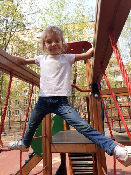 Fröhliches Mädchen klettert im Frühling auf dem Spielplatz auf die Seile und — Stockfoto