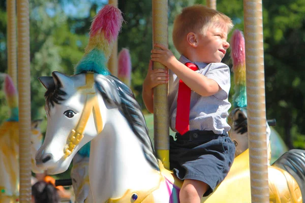 Little boy with a red tie riding a carousel — Stock Photo, Image