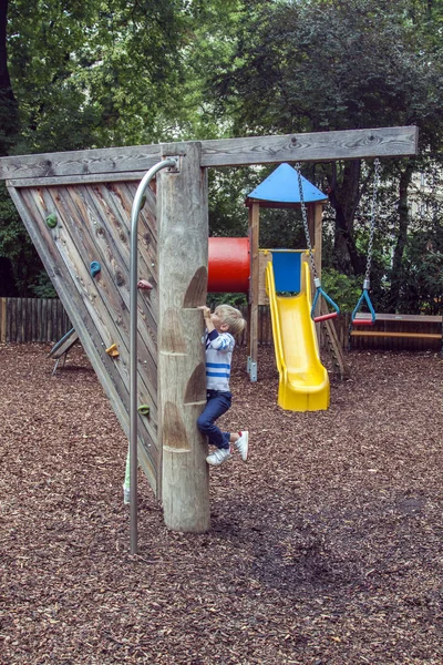 Menino sobe um poste de madeira com passos para deslizar para baixo um poste de fogo em um parque infantil ao ar livre moderno — Fotografia de Stock