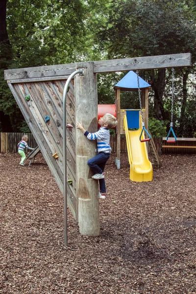 Menino sobe um poste de madeira com passos para deslizar para baixo um poste de fogo em um parque infantil ao ar livre moderno — Fotografia de Stock