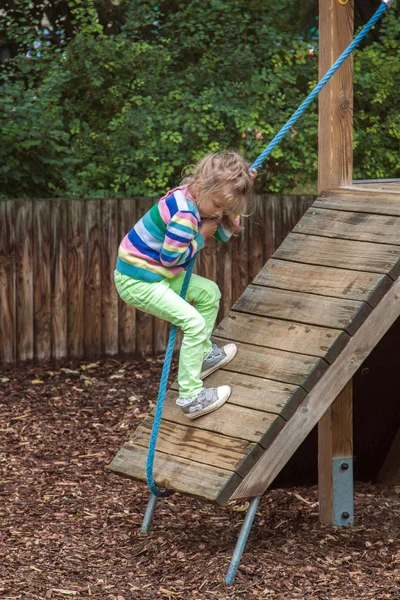 Menina sobe uma corda em uma inclinação de madeira em um parque infantil moderno ao ar livre — Fotografia de Stock