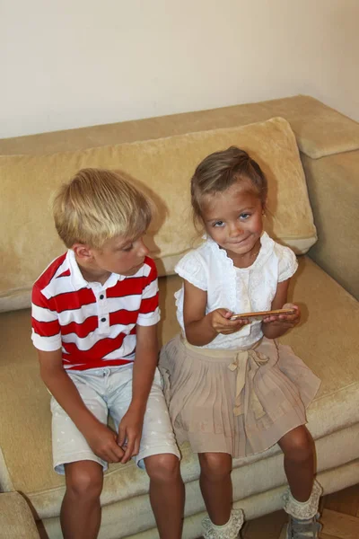 As crianças olham para a tela do smartphone. o menino olha para o telefone para a irmã feliz — Fotografia de Stock