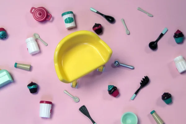 Platte lay afbeelding van plastic speelgoed servies met gebak en lege gele stoel op pastel roze achtergrond — Stockfoto