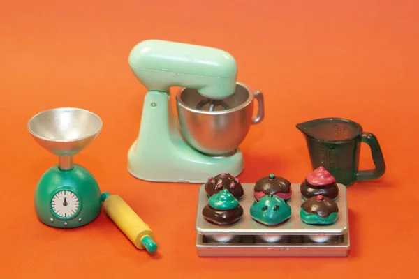 Máquina de cozinhar para preparar a massa, copo de medição, rolo, balanças, e os bolos acabados em um fundo laranja — Fotografia de Stock