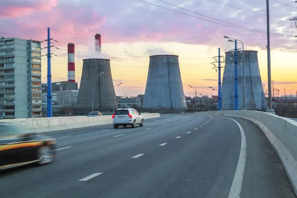 Road with cars passing in succession with heat power plant at su — ストック写真