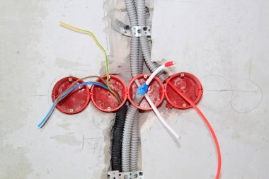 Yapım aşamasındaki evde elektriğe hazırlanmak için gri beton duvardaki deliklere elektrik kabloları ve kablolar yerleştirilmiş. Elektrik kablosu, duvardaki oyukta koruma kablosuna yerleştirilir.