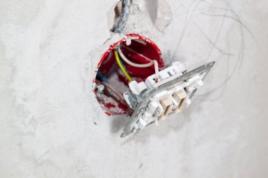 Çalılıktaki elektrik kablolarını ve kablolarını dışarı çıkararak, inşaat halindeki evde elektriğe hazırlanmak için gri beton duvarın içinde asılı duran prizlere bağladım..