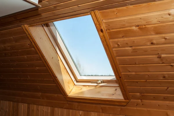 Closed dormer window in wooden house in the attic. Room has sloping ceiling made of natural eco-materials and views of park through window