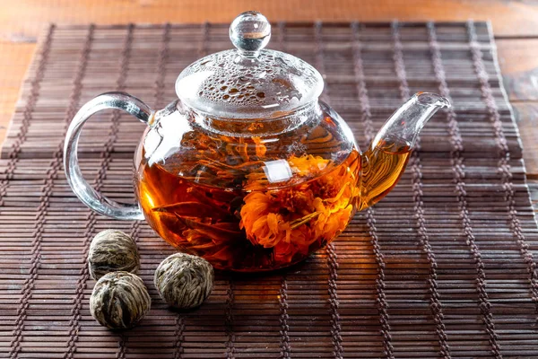 Tea in a glass teapot with a blooming large flower. Teapot with exotic green tea-balls blooms flower. Tea ceremony