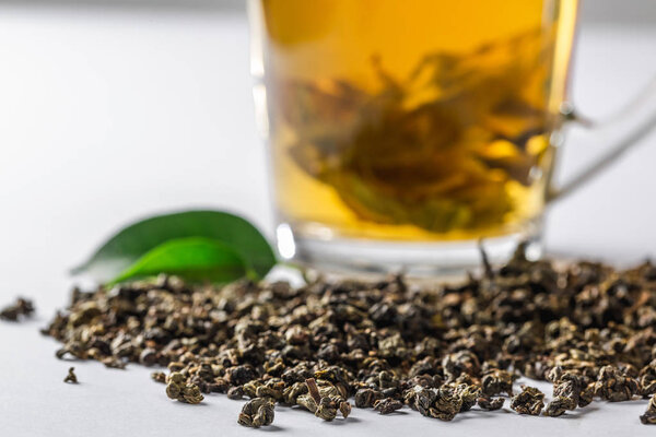Чашка зеленого чая с сушеным большим листом чая и свежими чайными листьями на белом фоне. Диета и здоровый напиток
