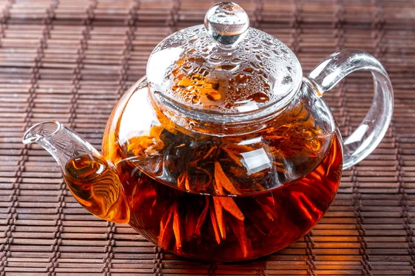 Tea in a glass teapot with a blooming large flower. Teapot with exotic green tea-balls blooms flower. Tea ceremony