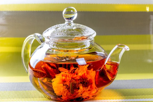 Chá em um bule de vidro com uma flor grande florescendo. Bule com flores exóticas de bolas de chá verde flor. Cerimônia de chá em fundo listrado verde — Fotografia de Stock
