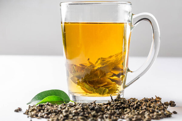 Чашка зеленого чая с сушеным большим листом чая и свежими чайными листьями на белом фоне. Диета и здоровый напиток
