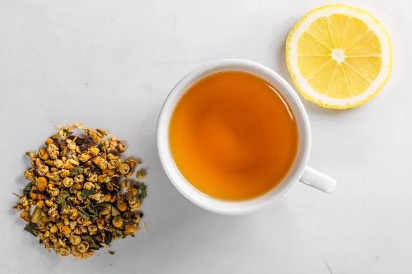 Una taza de té verde con flores secas de manzanilla y una rebanada de limón cortado sobre un fondo blanco. Dieta y bebida saludable. Flatley. Vista superior — Foto de Stock