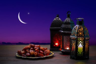 Ornamental dark Moroccan, Arabic lantern and dates on on an old wooden table with the night sky and the Crescent moon and the star behind. Greeting card for Muslim community holy month Ramadan Kareem. clipart