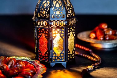 The Muslim feast of the holy month of Ramadan Kareem with dates on a tray on a dark background. Beautiful background with a shining lantern Fanus. clipart