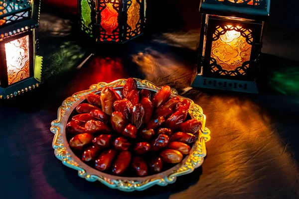 The Muslim feast of the holy month of Ramadan Kareem with dates on a tray on a dark background. Beautiful background with a shining lantern Fanus.