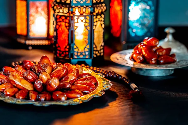 The Muslim feast of the holy month of Ramadan Kareem with dates on a tray on a dark background. Beautiful background with a shining lantern Fanus.