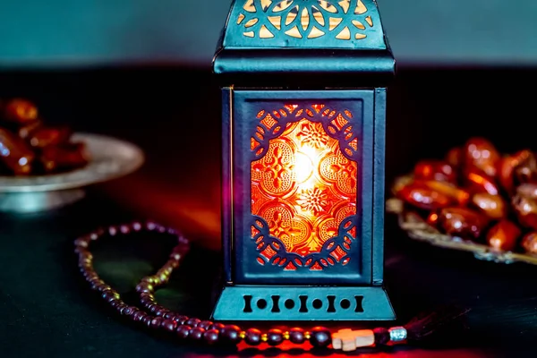 The Muslim feast of the holy month of Ramadan Kareem with dates on a tray on a dark background. Beautiful background with a shining lantern Fanus.