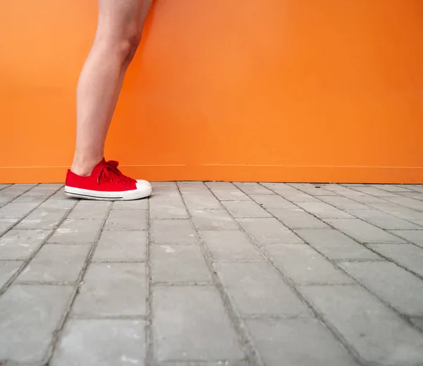 Mooie lange benen van vrouw poseren buiten in de zomer de stijl van de sport van de hipster van de sensuele manier op oranje muur achtergrond in rode sneakers — Stockfoto