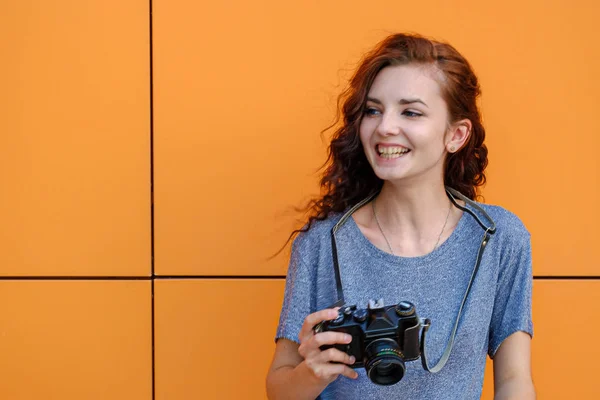 A divatos fiatal fotós, mosolygós, vintage film fényképezőgép a kezében, narancssárga fal előtt álló — Stock Fotó