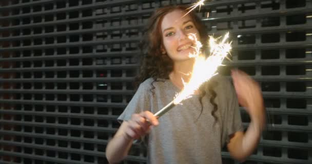 Slowmo footage of teenage girl with sparkler in her hands in front of metal fence — Stock Video