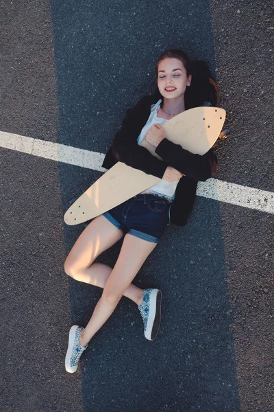 Дівчина лежить зі своєю дошкою на асфальтовій поверхні вулиці — стокове фото