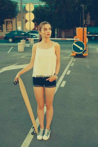 Mulher na rua vintage moda desgaste de pé no estacionamento na frente de sinais de estrada e olhando para longe enquanto segurando longboard — Fotografia de Stock